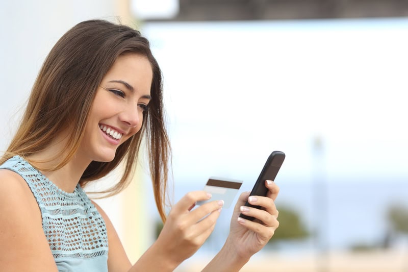 Portrait of a happy woman buying online with a smart phone outdoors